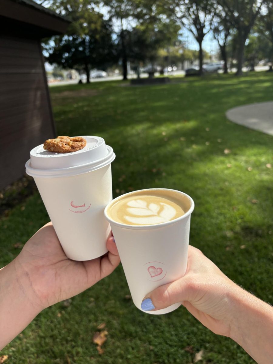 Two hands holding Lady Blume's fall creations in La Plaza Park on a crisp, sunny Fall day! On the left, a hot Cajeta latte is topped with a mini chocolate chip cookie. Next to it is a hot Wildflower latte with the lid off. Wednesday, Oct. 9, in Cotati. 