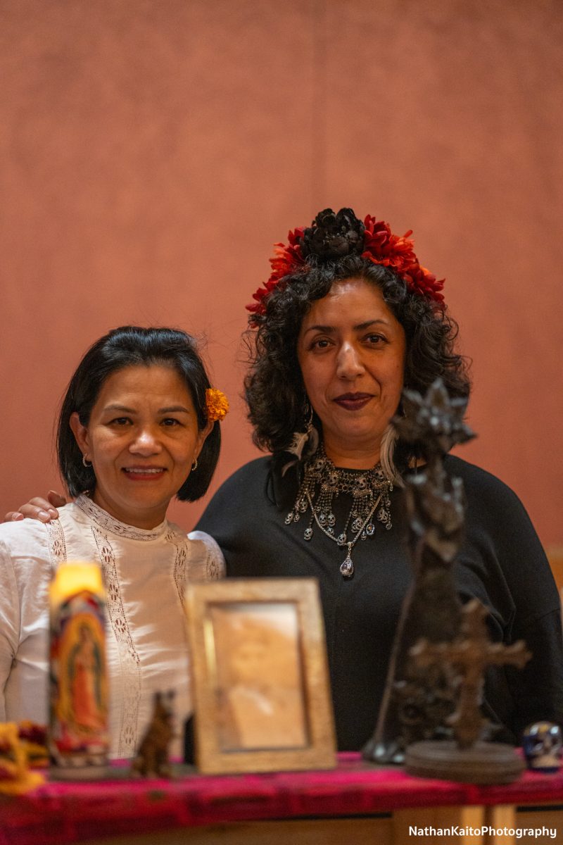 Erika Garcia and Elvira Barbosa pose in front of one of the altars decorated in the Bertolini Student Center  for the Dia De Los Muertos festivities on Wednesday, Oct. 23.