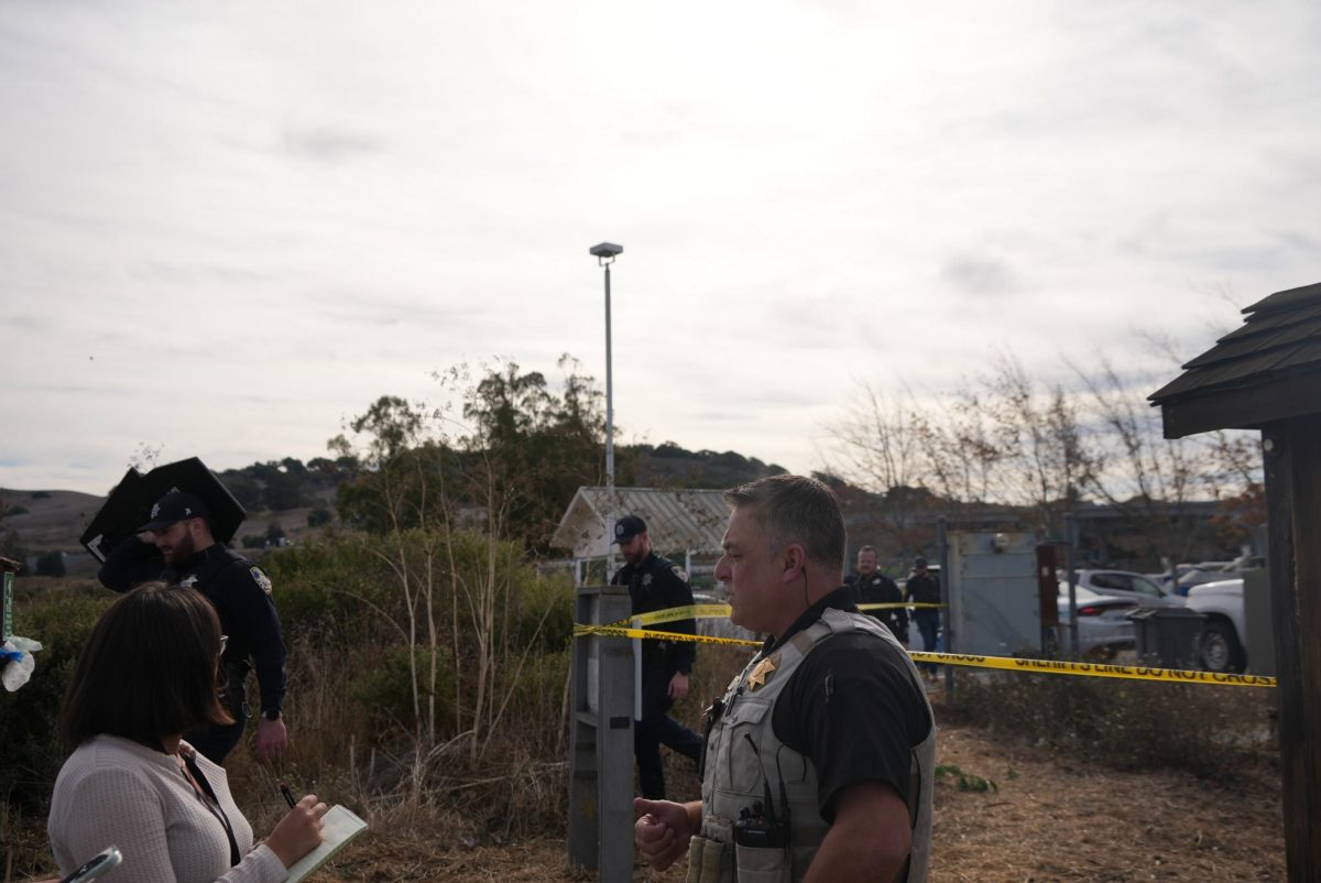 Sheriff's Deputy Rob Dillion briefing reporters on the scene along the Petaluma River behind the Sheraton Hotel. They were waiting for the suspect to surrender. Petaluma Police Officers walking in the background towards the riverbank on Tuesday, Nov. 5.