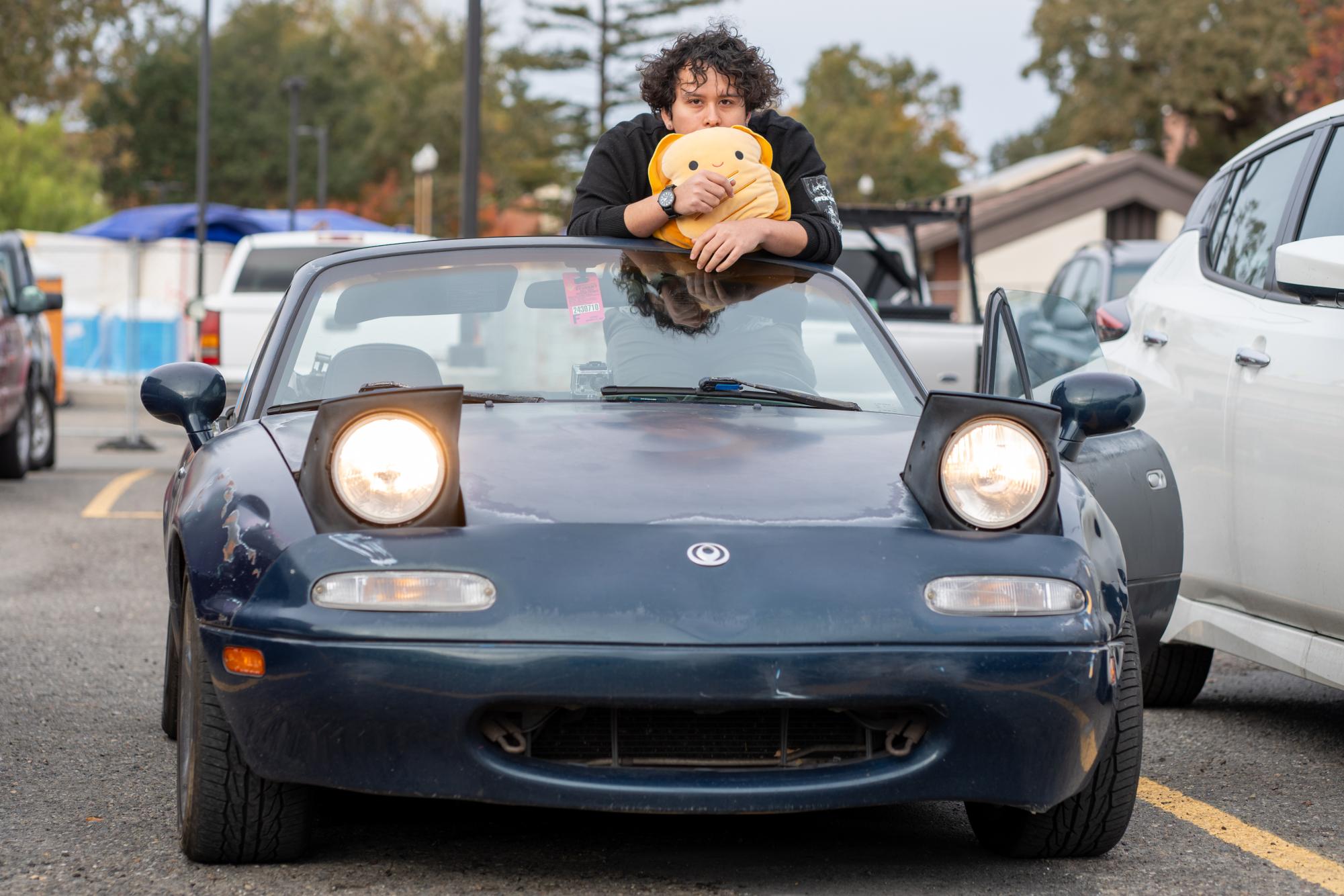 Oak Leaf Reporter Adair Rodriguez poses with a grilled-cheese plush in his 1995 Mazda Miata in the Quinn parking lot on Nov. 19, 2024.