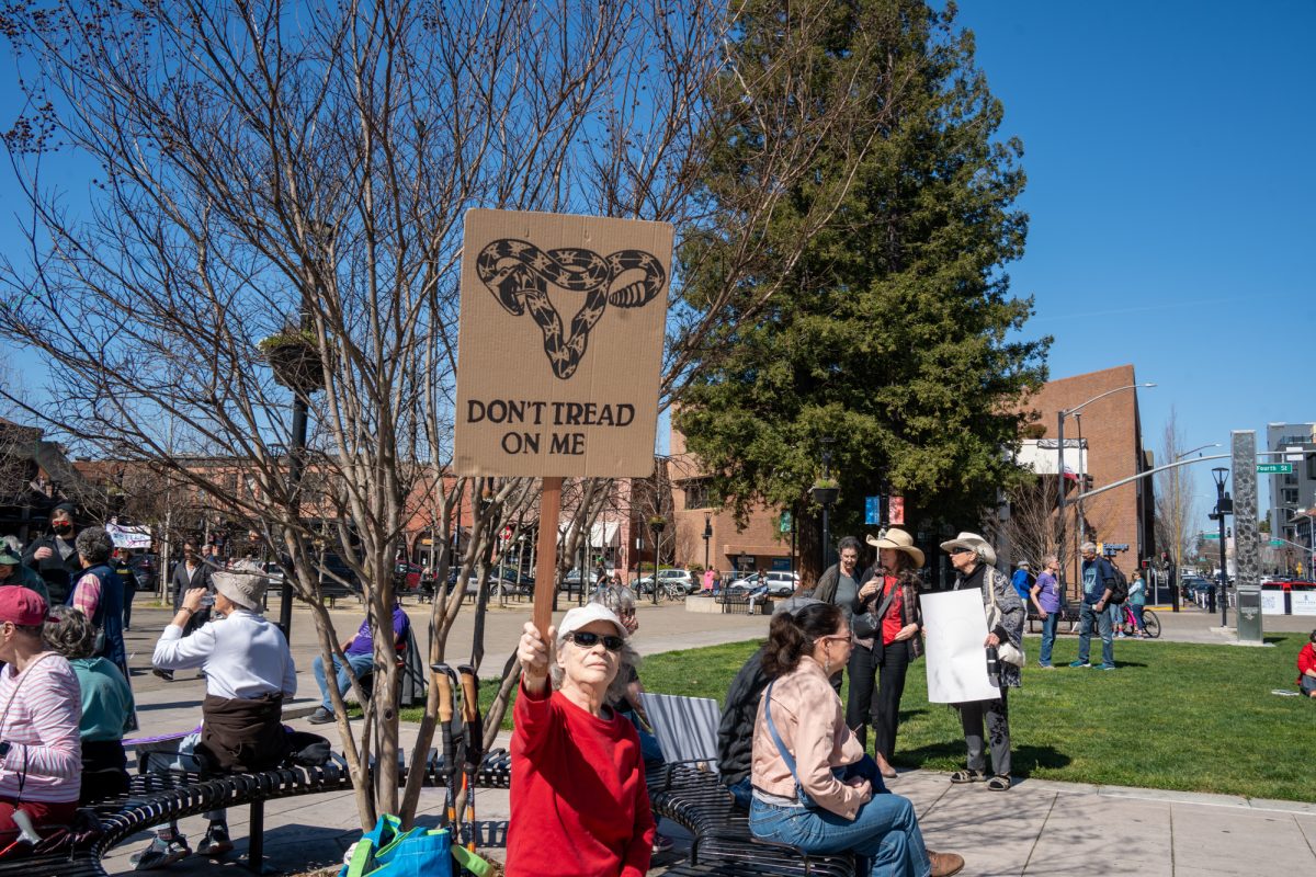 A demonstrator holds a sign reading " Don't Tread On Me" while sitting at a bench during the International Women’s Day march in Old Courthouse Square on Saturday, March 8, 2025 in Santa Rosa.  