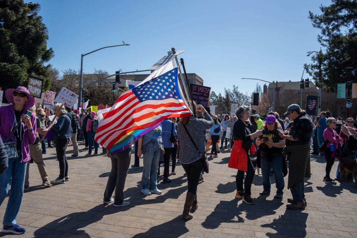 A demonstrator carries flags through the crowd during the International Women’s Day march in Old Courthouse Square on Saturday, March 8, 2025 in Santa Rosa.  