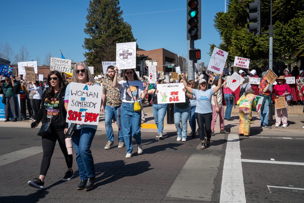 Demonstrators cross the street towards Santa Rosa Avenue during the International Women’s Day march in Old Courthouse Square on Saturday, March 8, 2025 in Santa Rosa.  